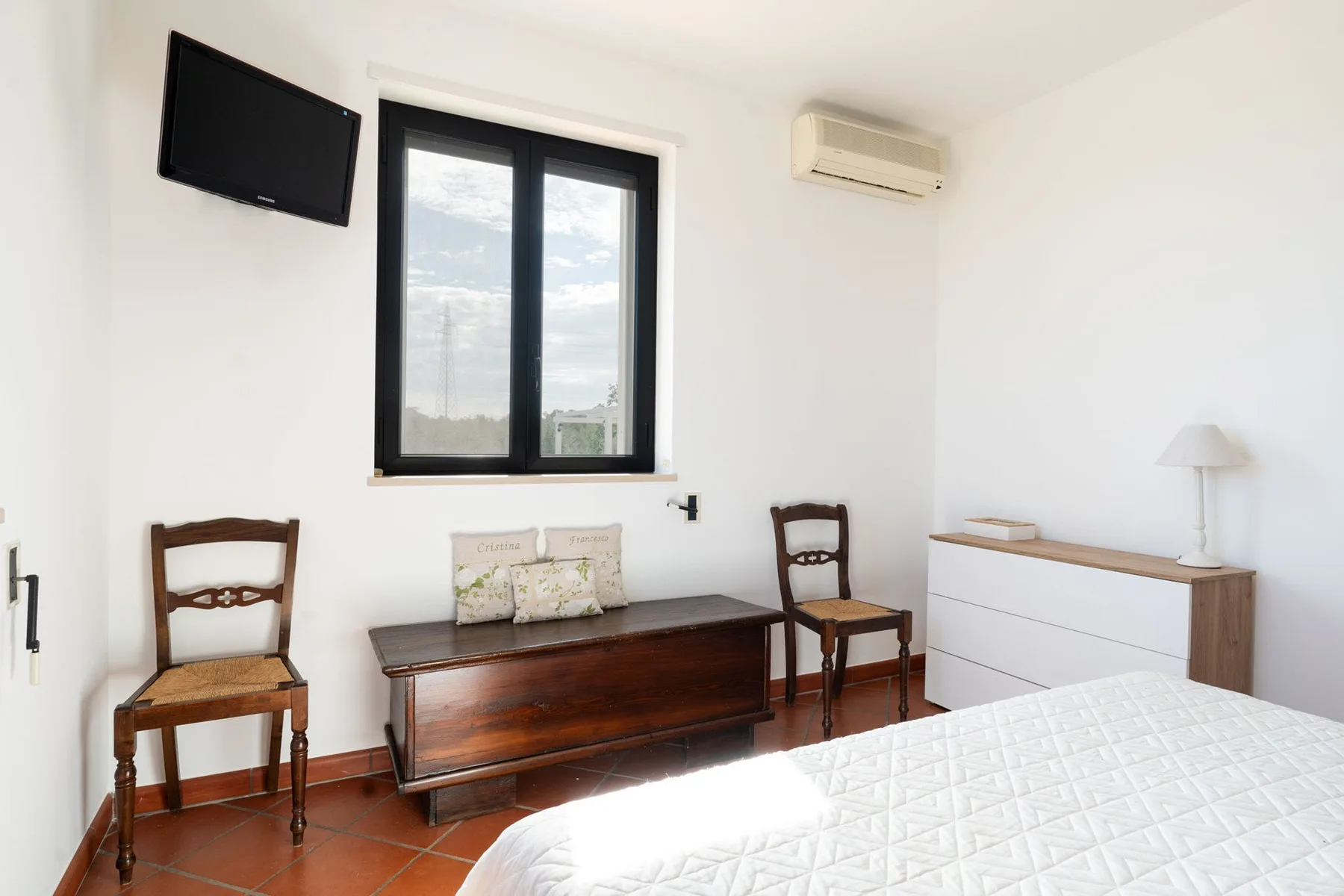Un dormitorio con una cama, asientos de madera y una ventana.