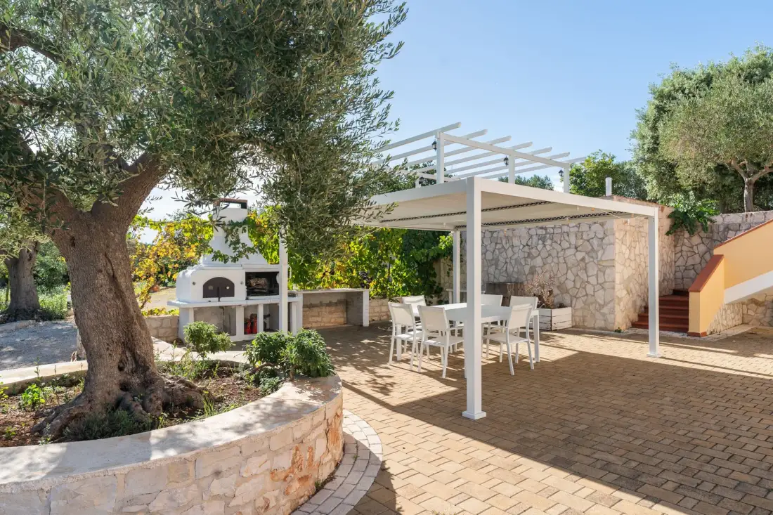 Patio exterior pavimentado con pérgola, mesa de comedor y barbacoa empotrada.