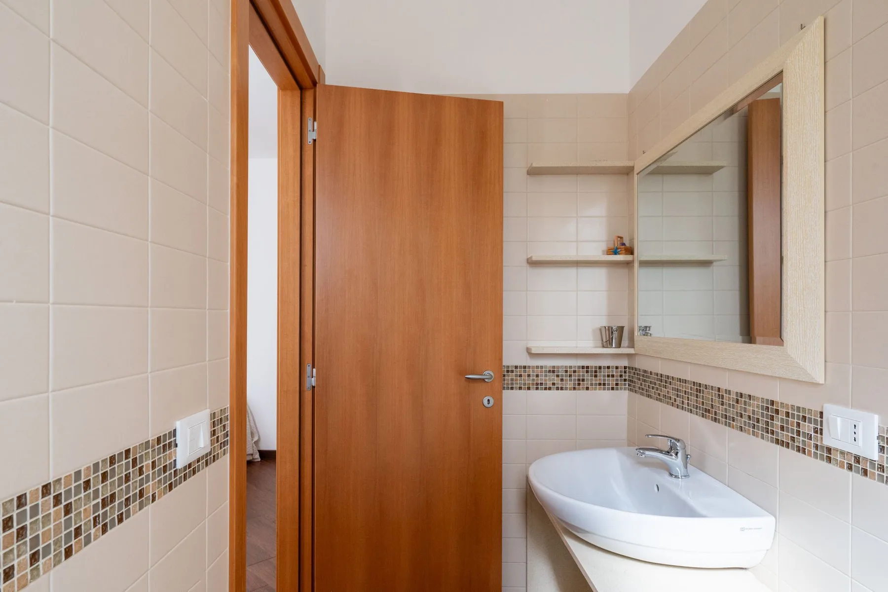 Un baño alicatado con lavabo, espejo y puerta de madera abierta.