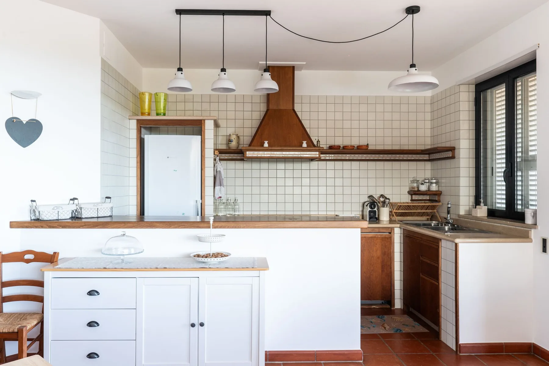 Una cocina luminosa con una isla central, paredes de azulejos y gabinetes de madera oscura.