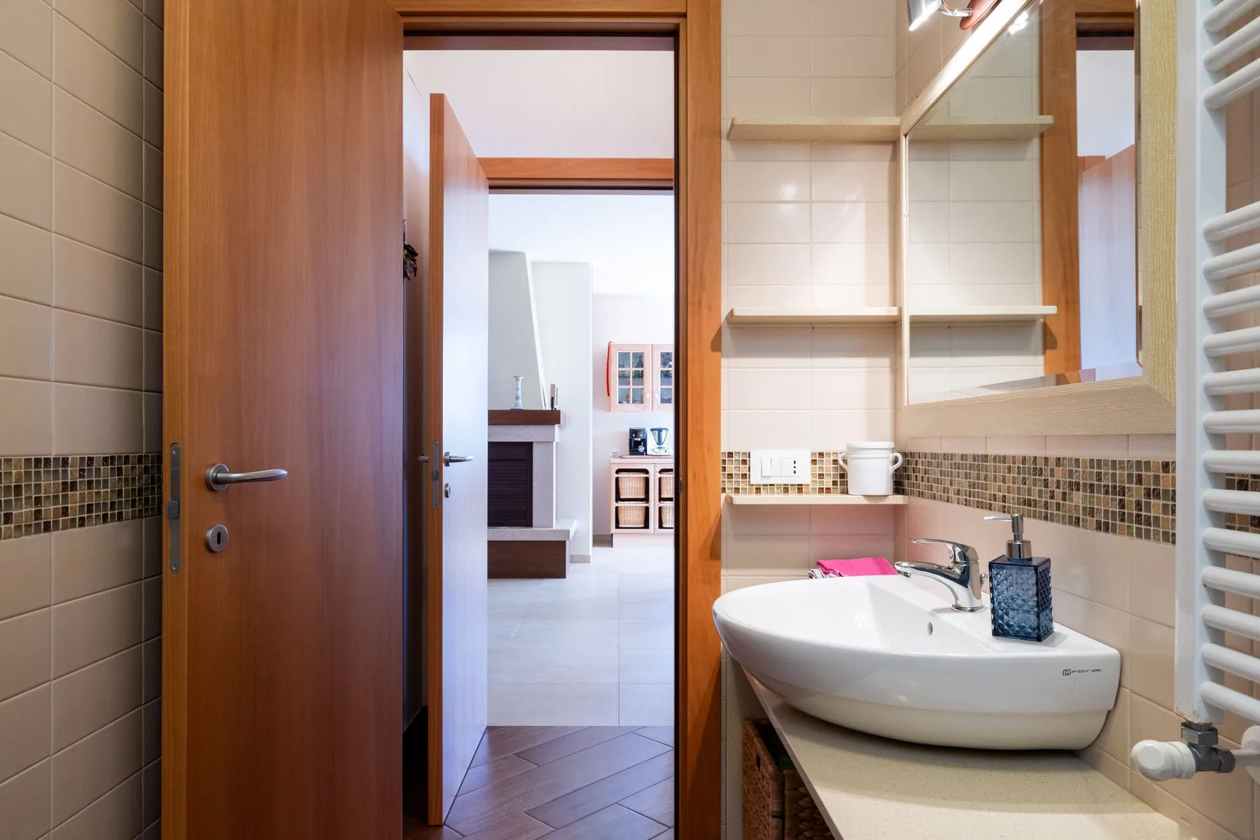 Un baño con azulejos, un lavabo blanco y una puerta de madera abierta a otra habitación.