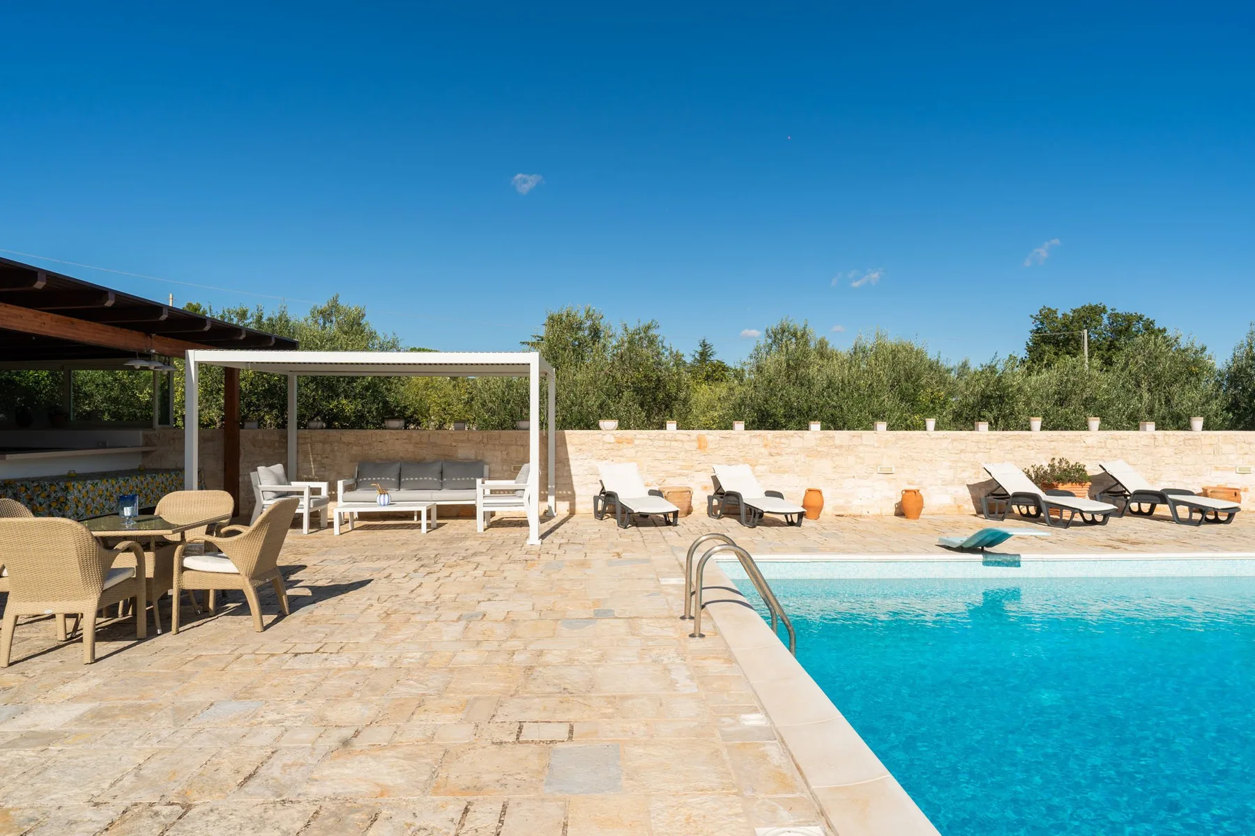 Una piscina al aire libre junto a un patio pavimentado con asientos.