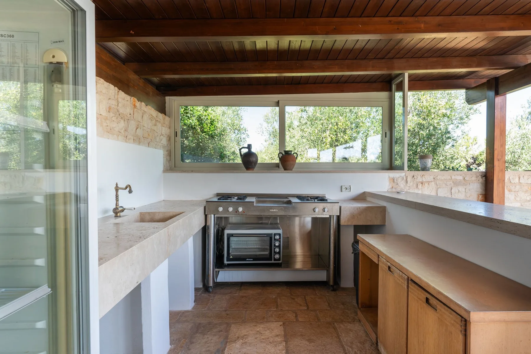 Una cocina rústica con encimeras de piedra, gabinetes de madera y ventanas con vistas a la vegetación.