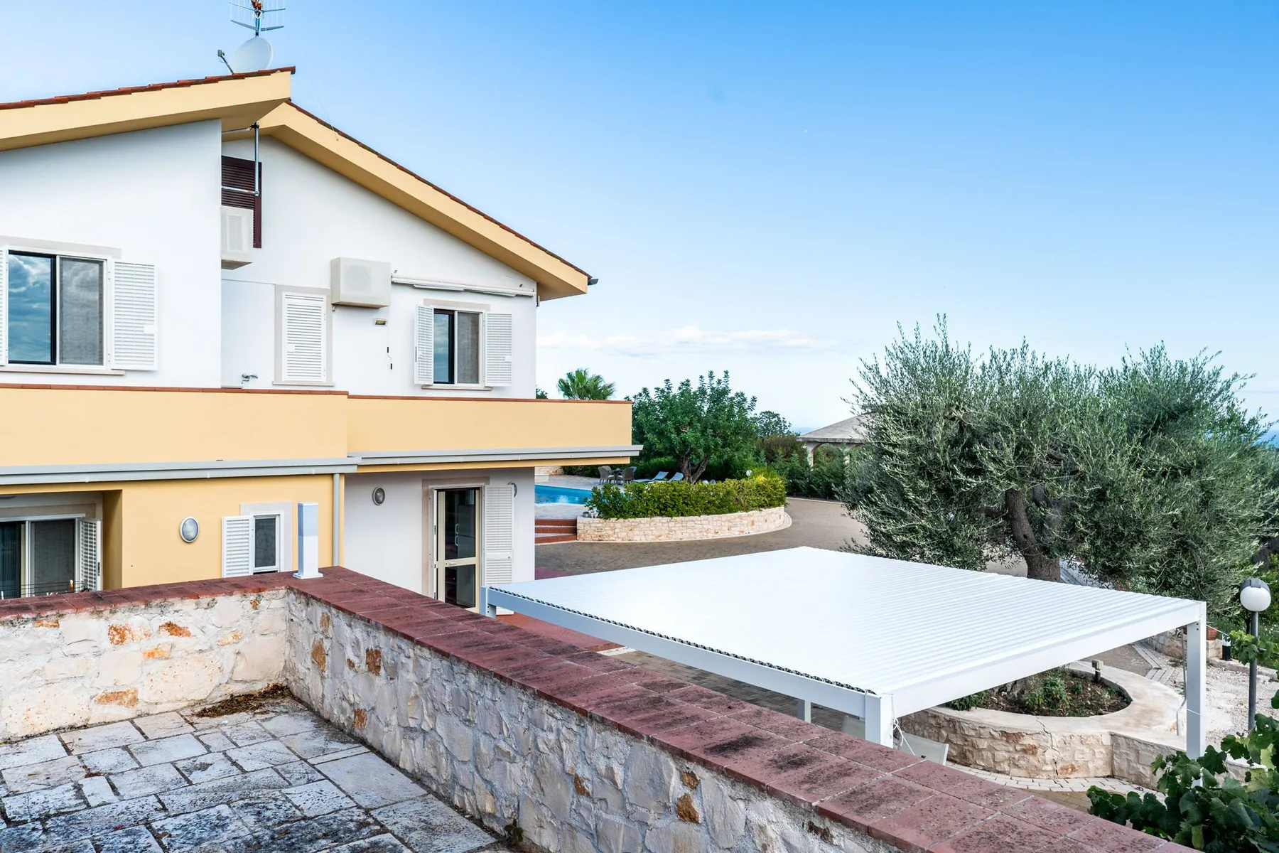 Una casa blanca con un patio cubierto y un muro de piedra en primer plano.