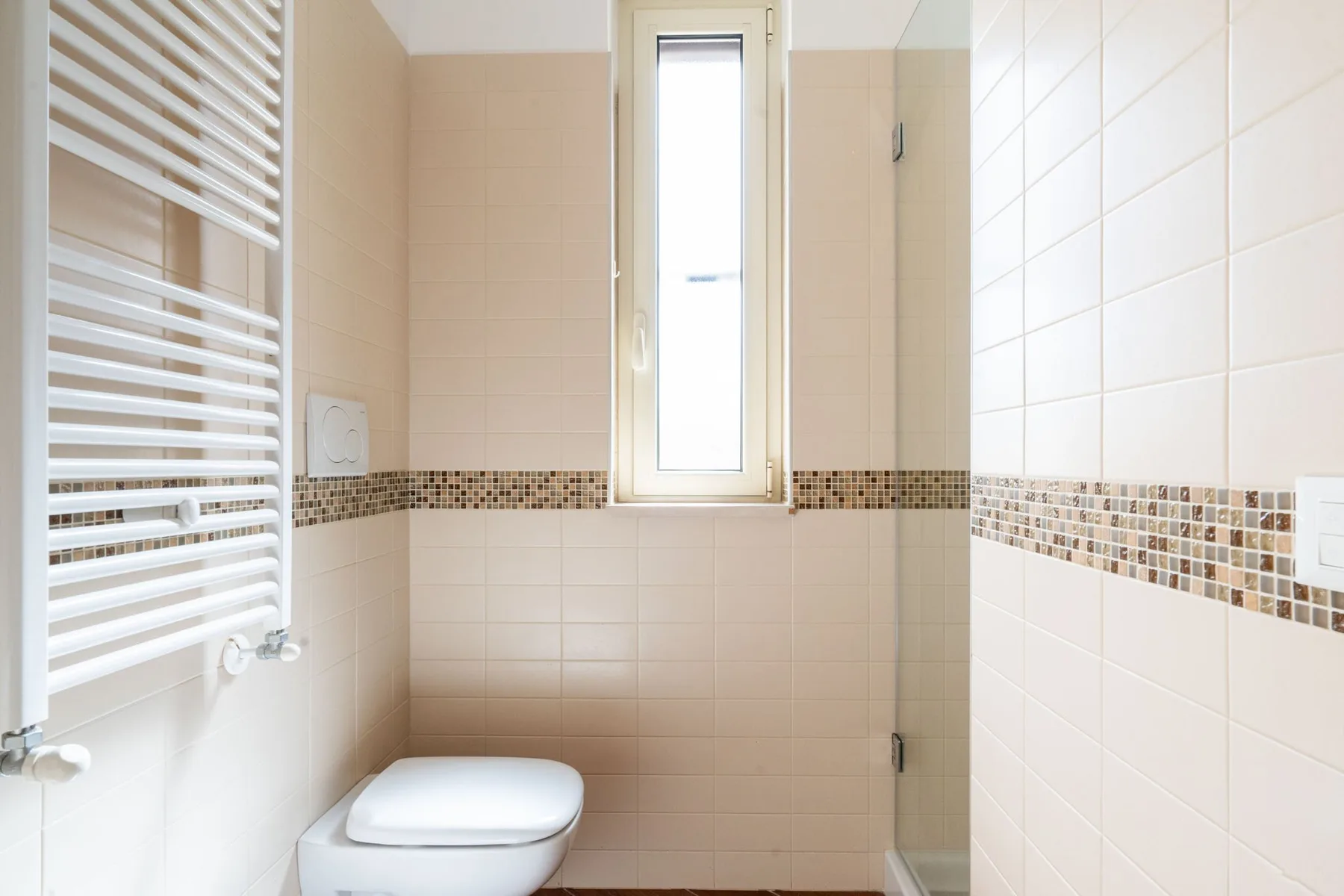 Baño alicatado con una ventana estrecha y un radiador toallero de pared.