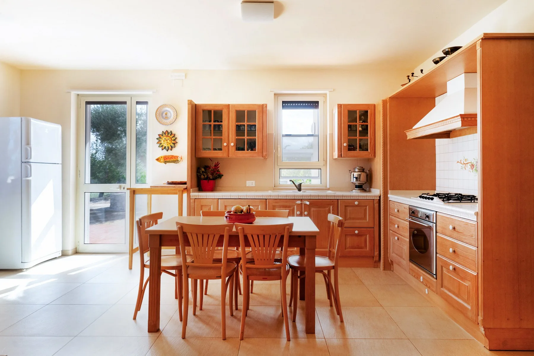 Una cocina luminosa con gabinetes de madera, una mesa de comedor y ventanas grandes.
