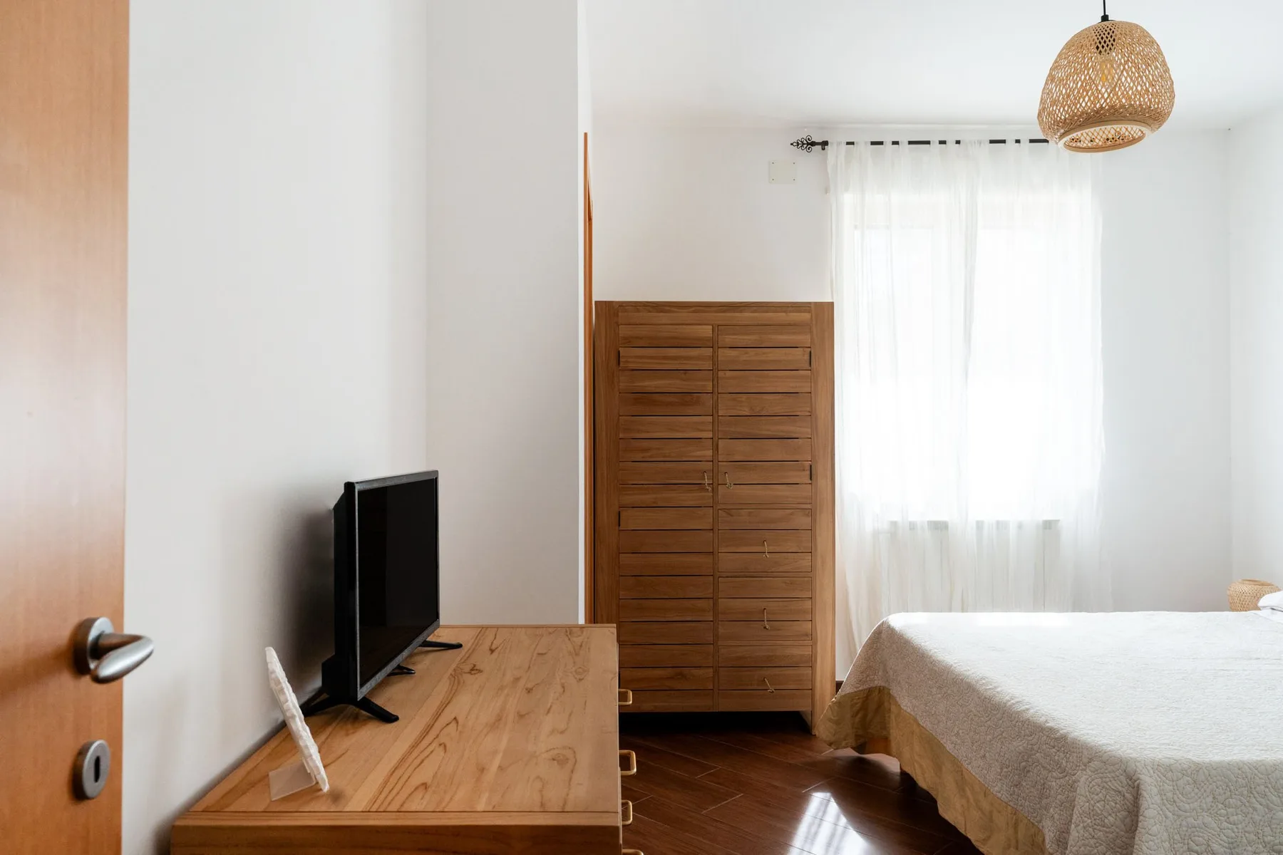 Un dormitorio con una cama, una cómoda de madera y un televisor sobre un escritorio.