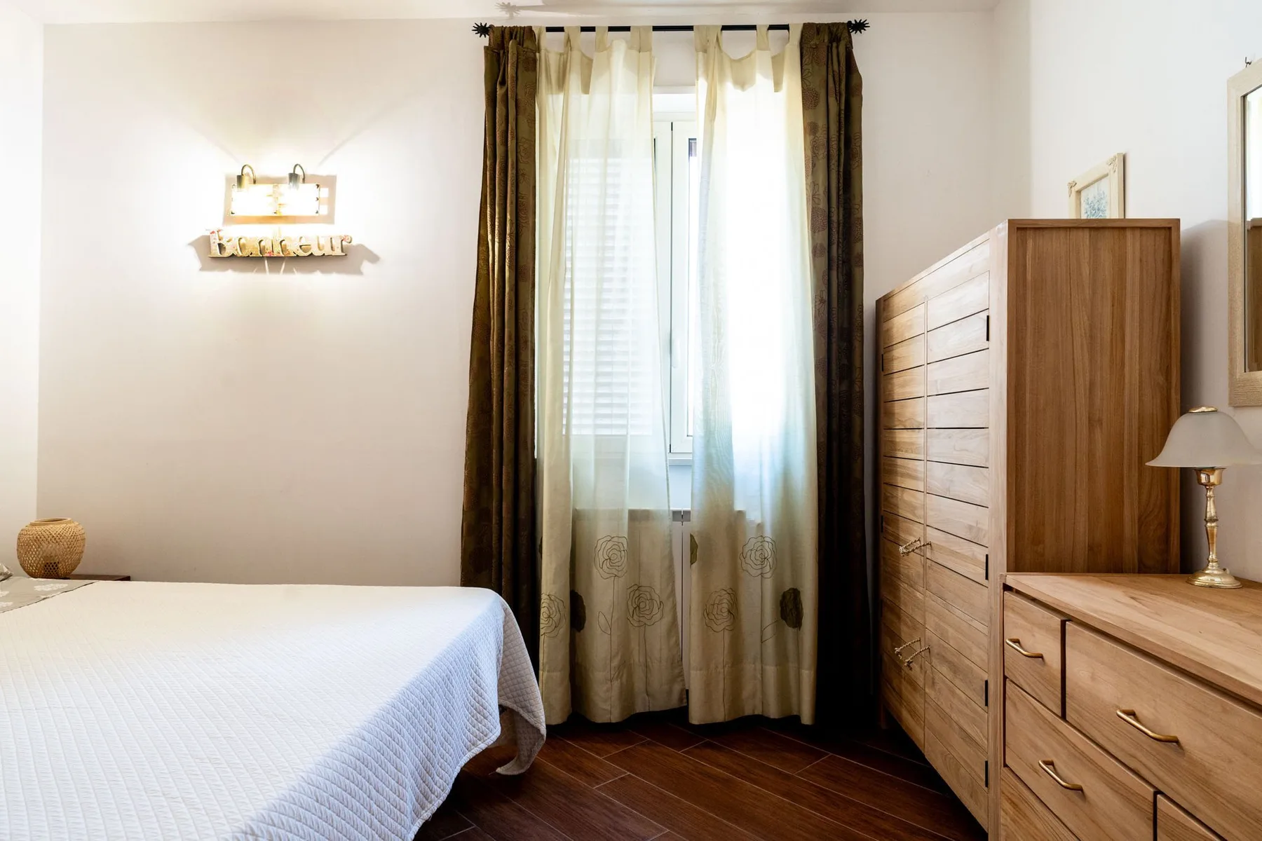 Un dormitorio con una cama, una ventana con cortinas y cómodas de madera.