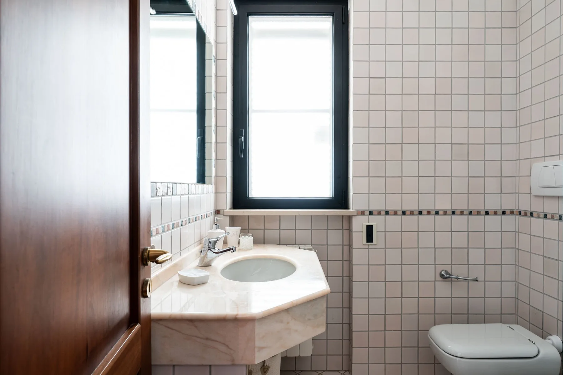 Un baño con azulejos, lavabo, inodoro y ventana.