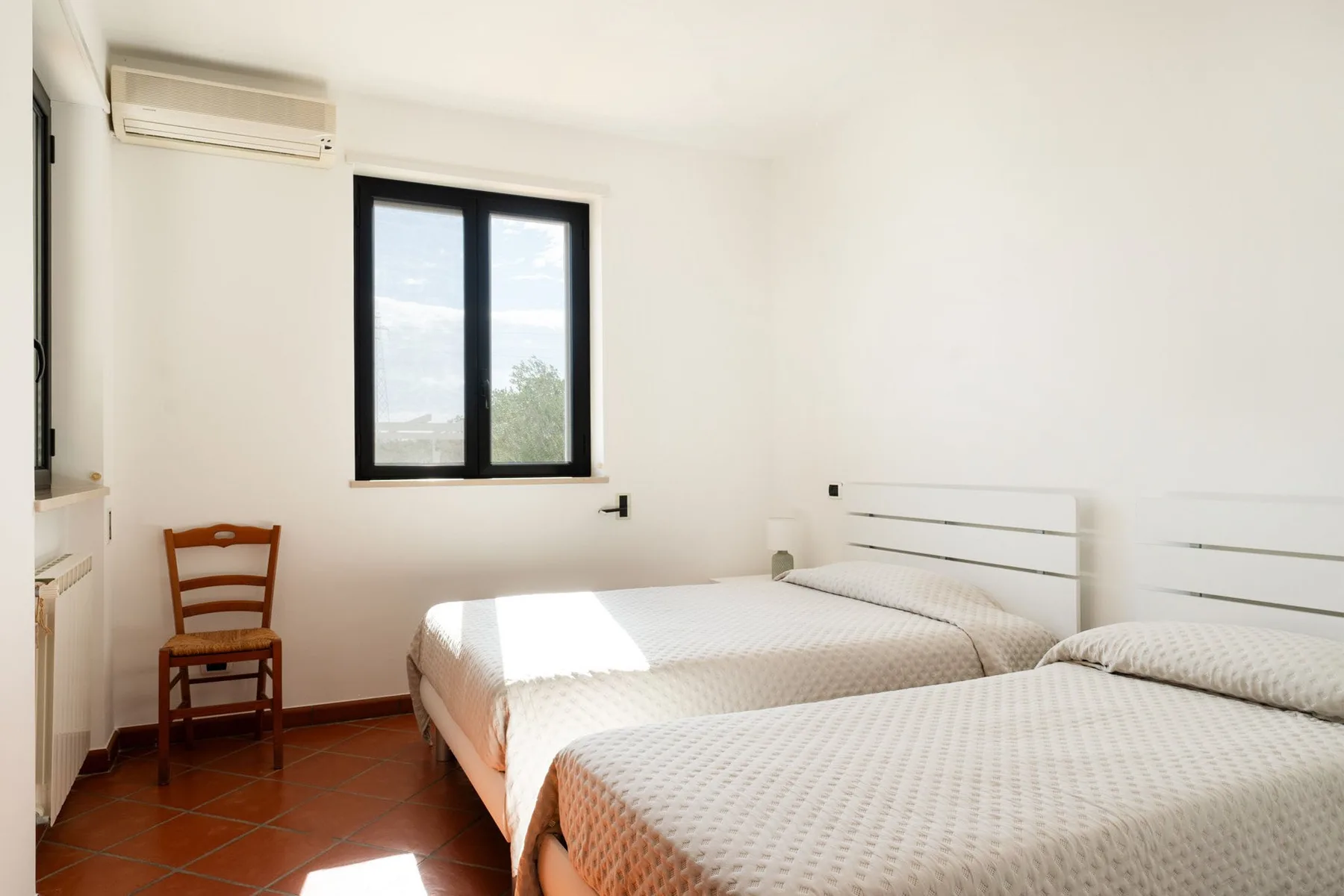 Un dormitorio con dos camas, una ventana y una silla de madera.