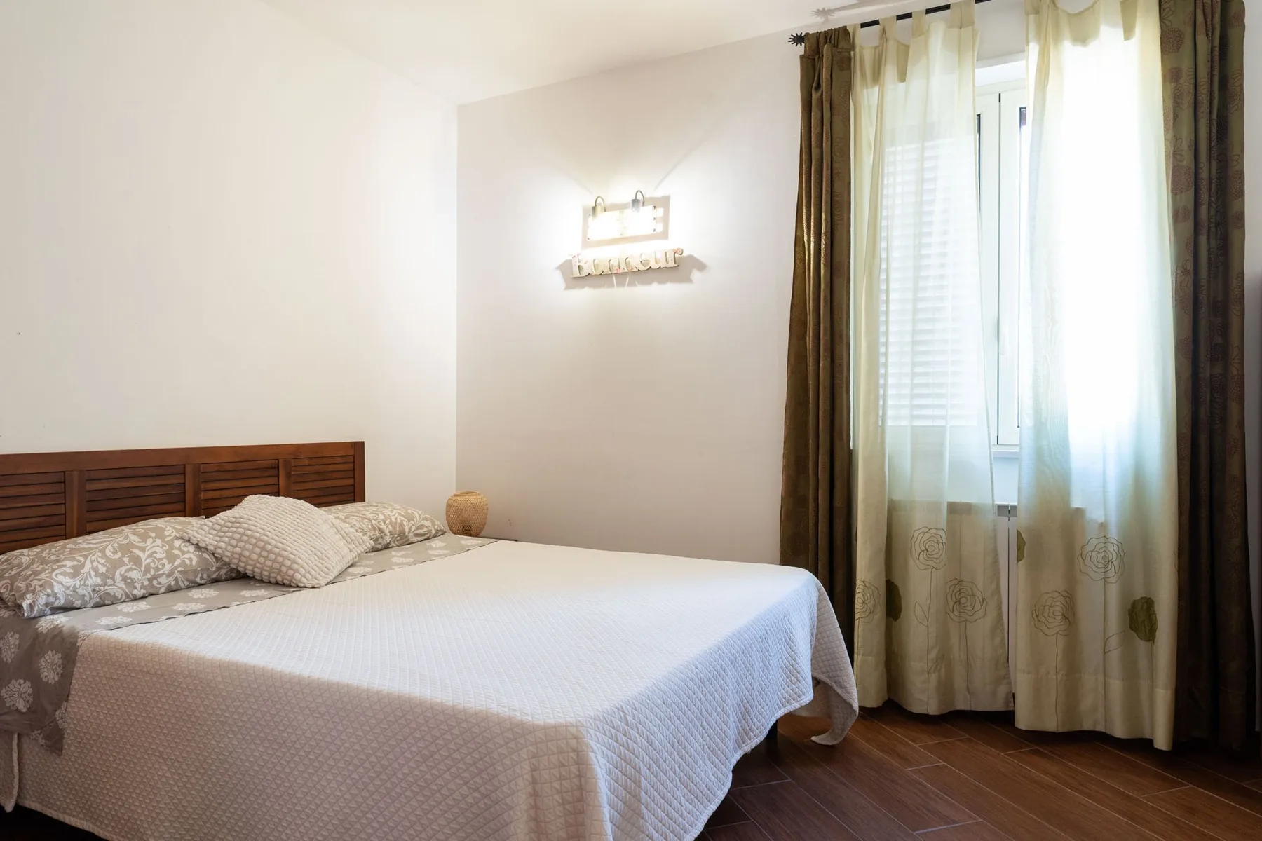 Un dormitorio con una cama bien tendida junto a una ventana con cortinas.