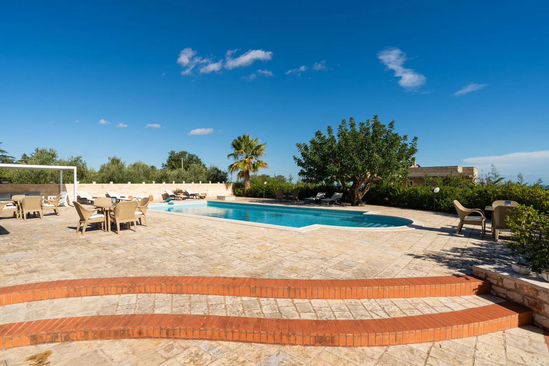 Una piscina al aire libre junto a un patio pavimentado con asientos.