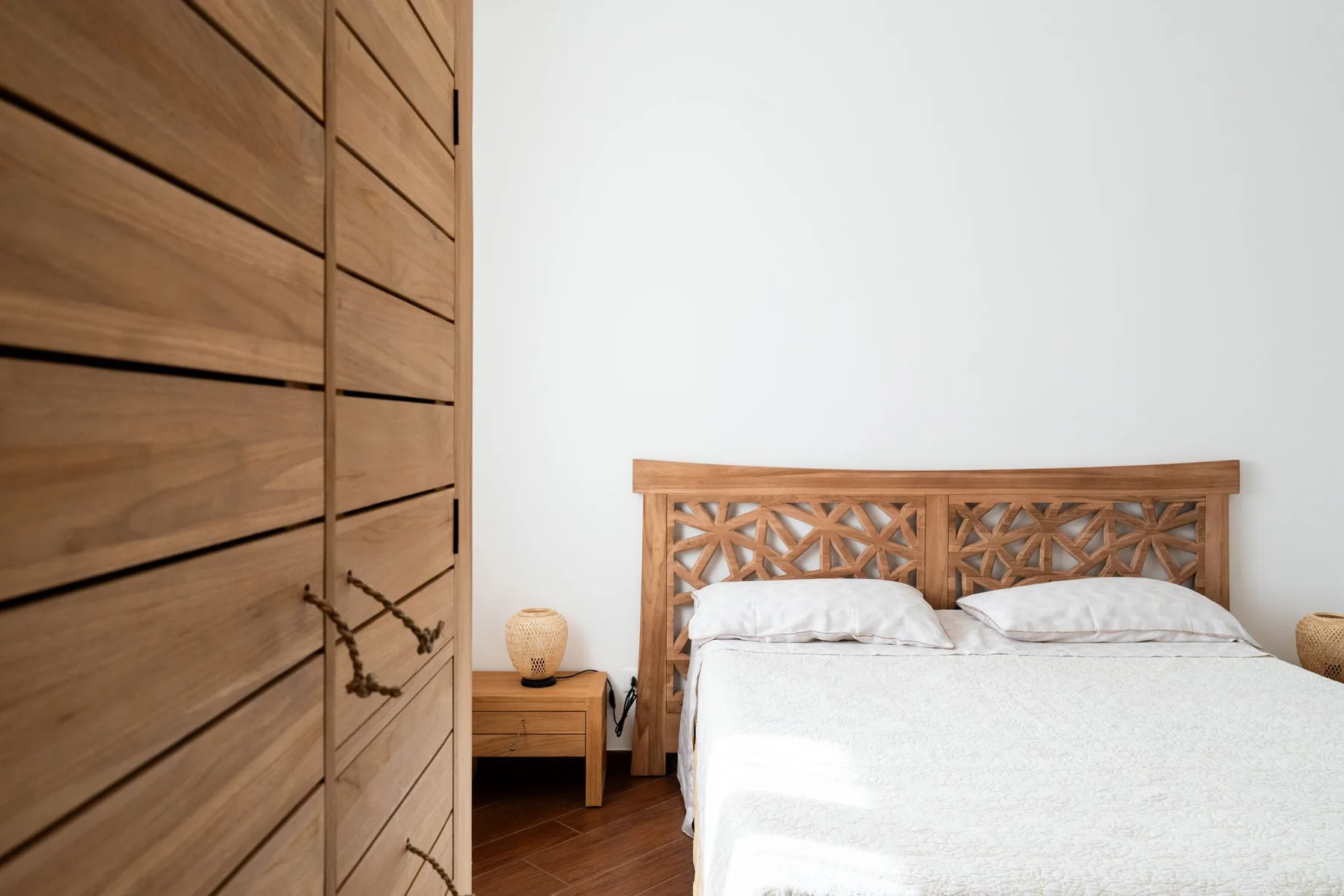 Un dormitorio con una cama blanca y un cabecero de madera tallada.
