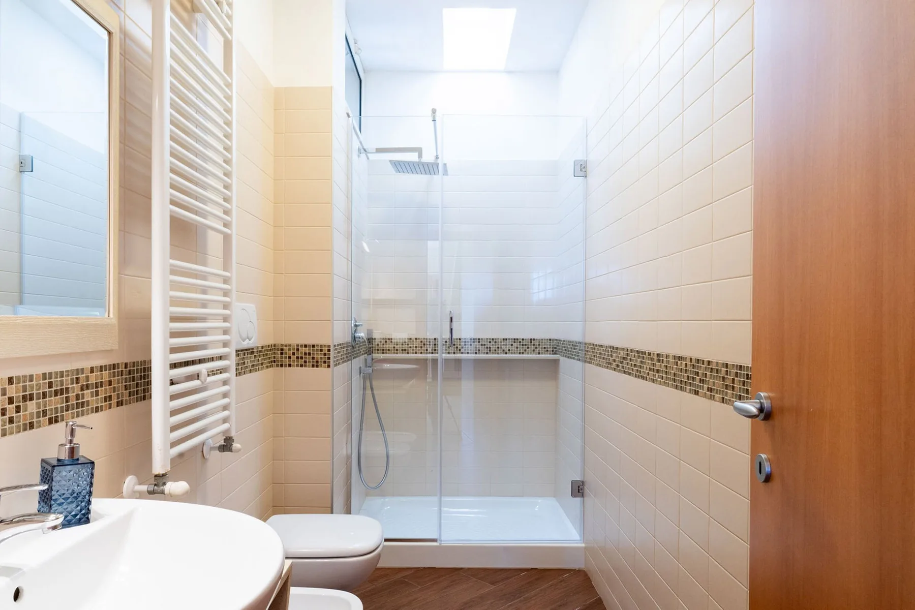 Un baño alicatado tiene una ducha de vidrio y un lavabo blanco.