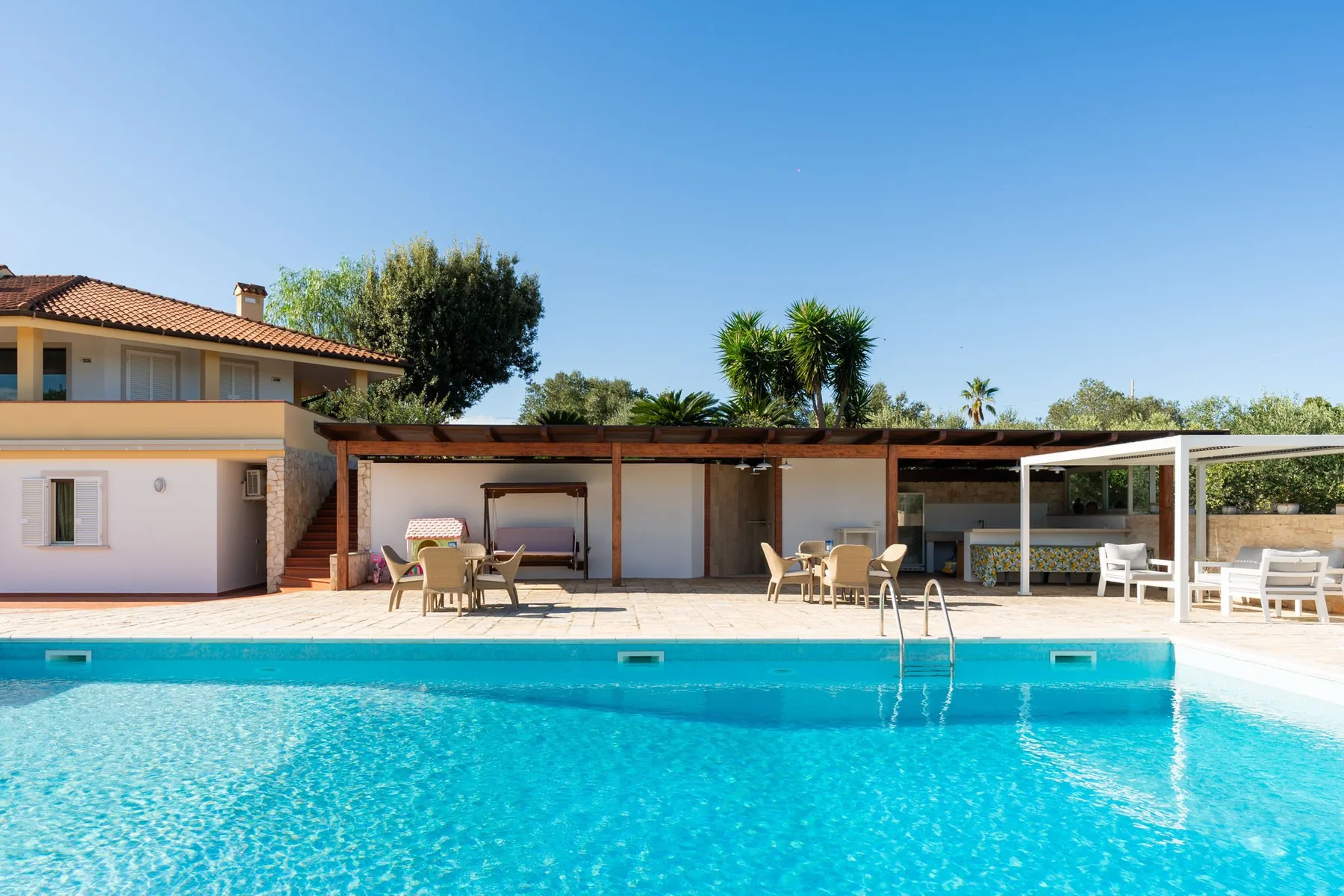 Una piscina al aire libre está frente a un patio sombreado con asientos.