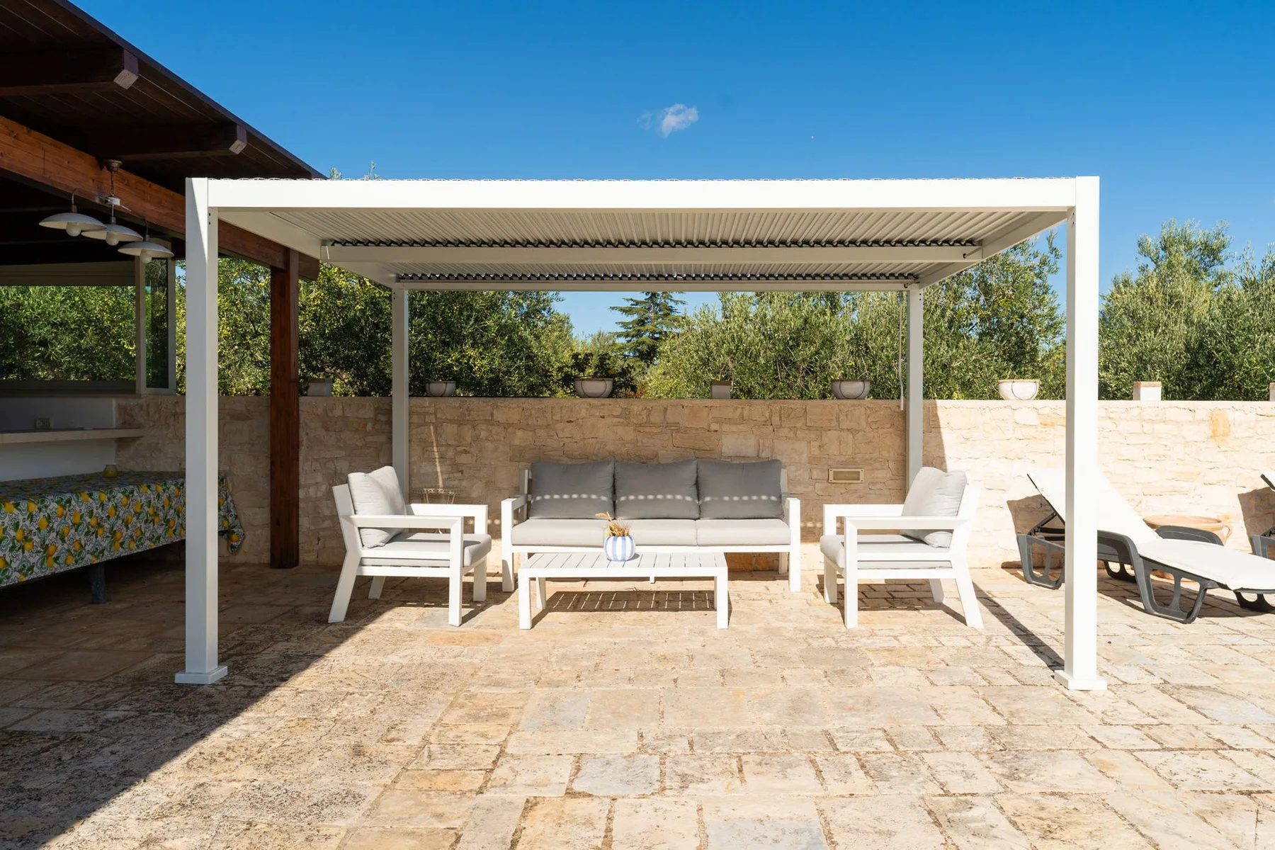 Un patio pavimentado tiene una zona de estar a la sombra bajo una pérgola.