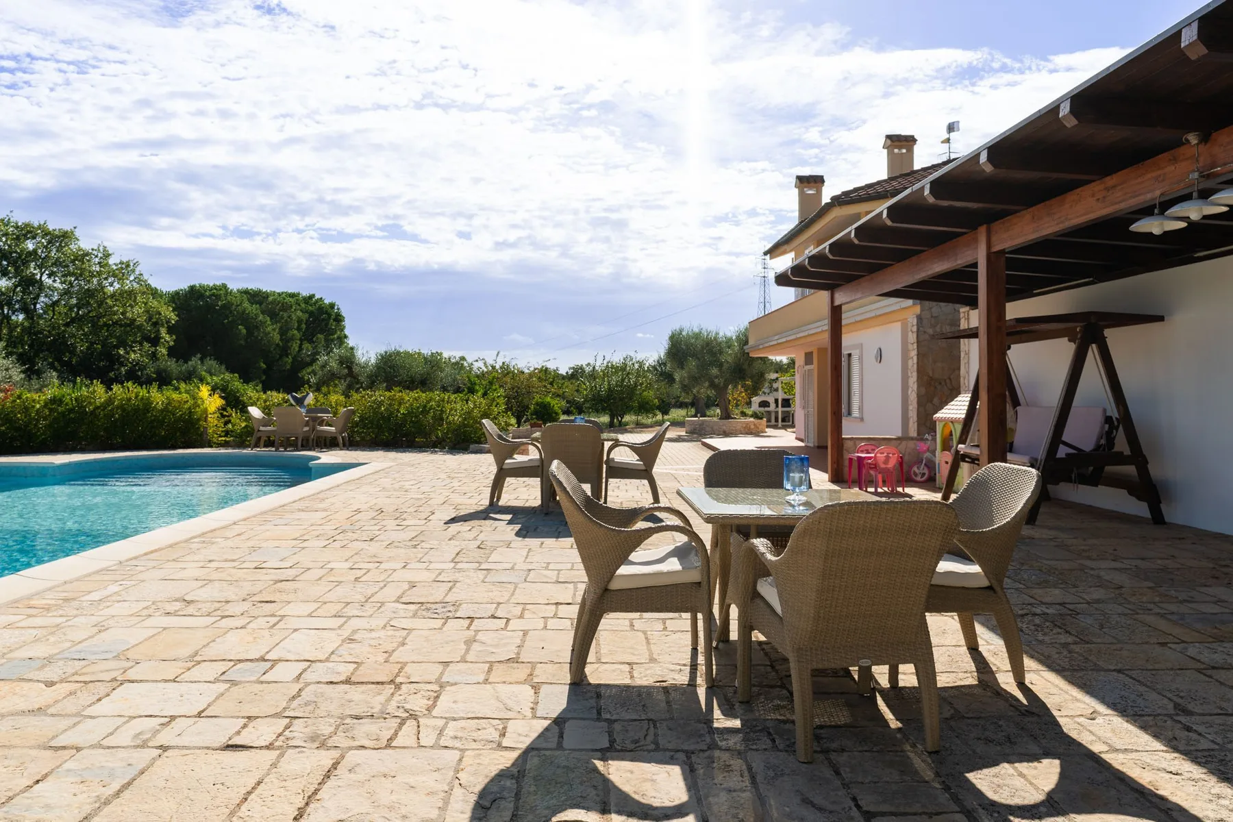 Un patio pavimentado con asientos junto a una piscina y una estructura cubierta.