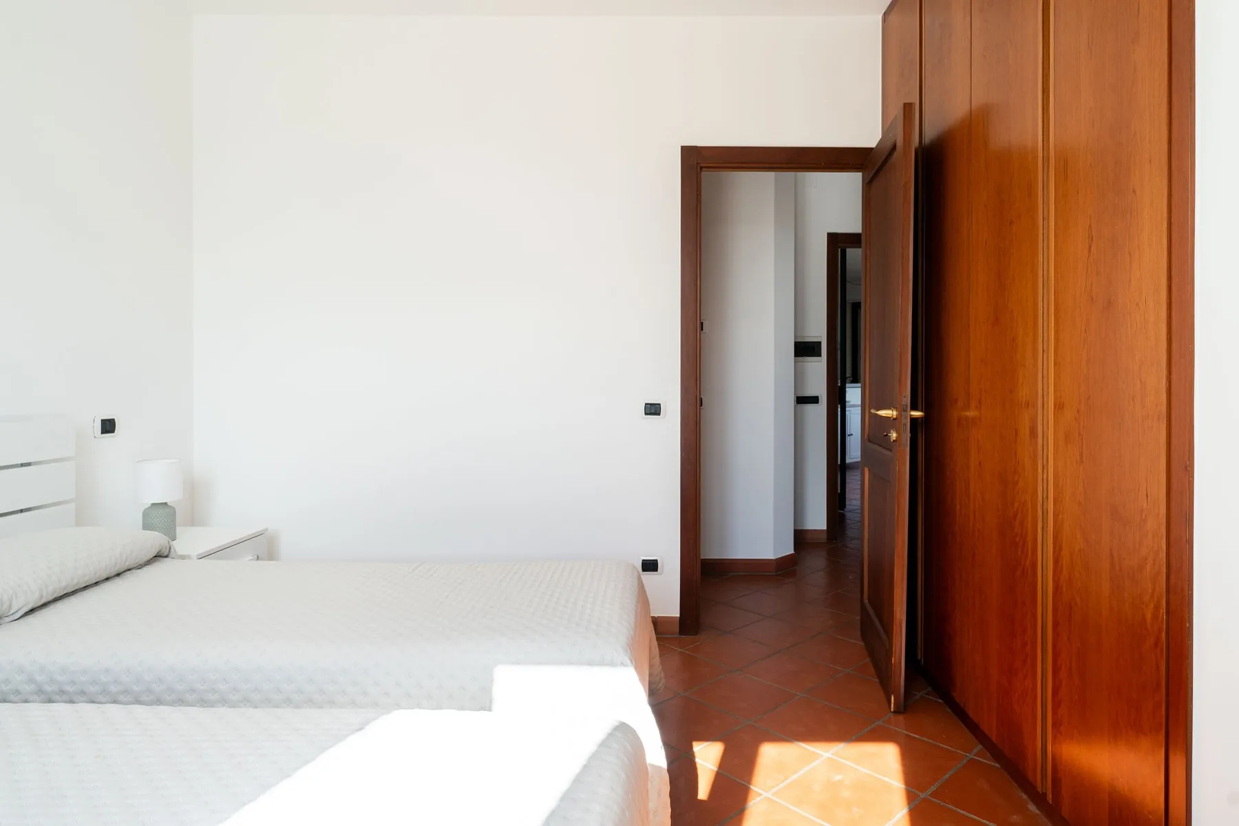Un dormitorio luminoso con ropa de cama blanca y un armario de madera.
