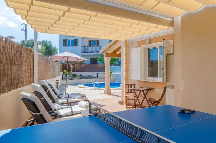 A shaded patio overlooks a swimming pool, with lounge seating and a table tennis table.