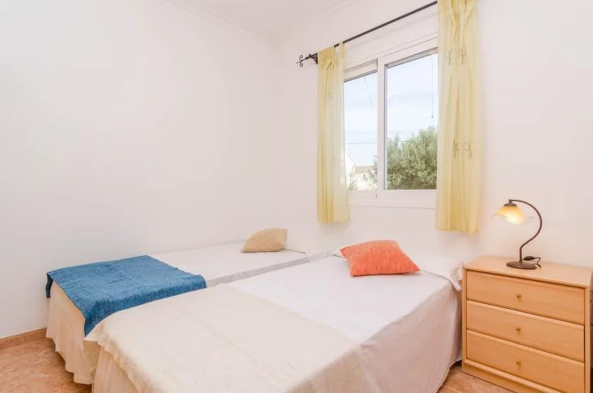 A bright bedroom with beds beside a window and a wooden dresser.