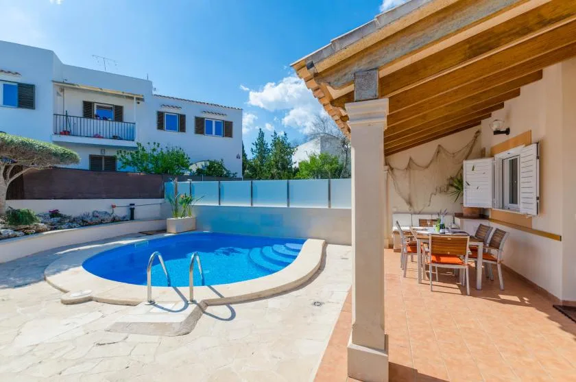A swimming pool beside a covered patio with outdoor dining furniture.