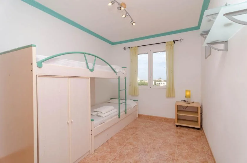 A bedroom with bunk beds, a window, and a small bedside cabinet.