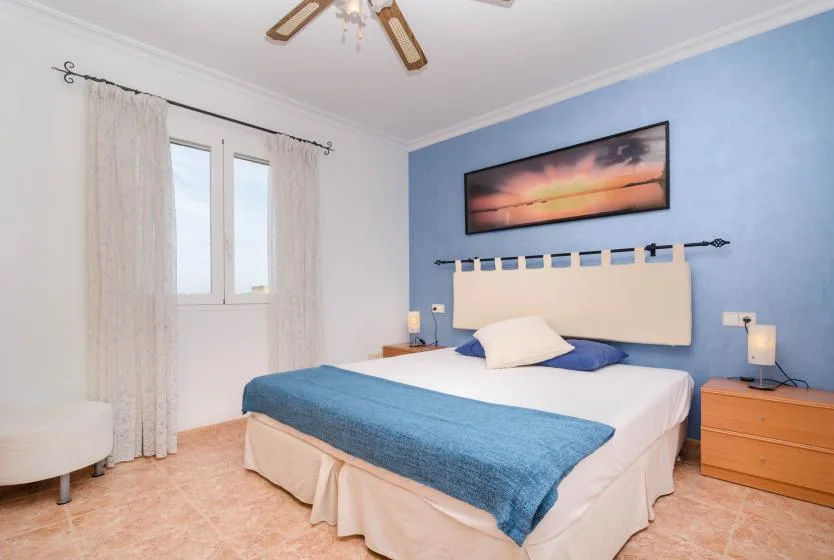 A bedroom with a bed dressed in white and blue bedding against a blue wall.