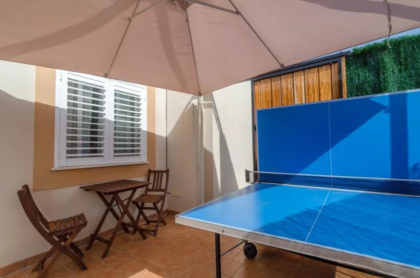 A covered outdoor table tennis area with a small seating table beside it.
