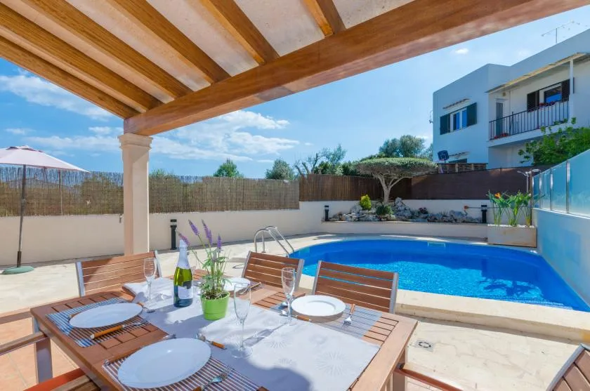 A covered patio dining area beside a swimming pool, with a table set for a meal.