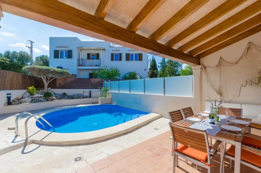 A covered patio with outdoor seating overlooks a blue swimming pool.