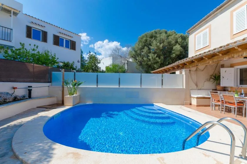 An outdoor swimming pool sits between two houses, with patio seating nearby.
