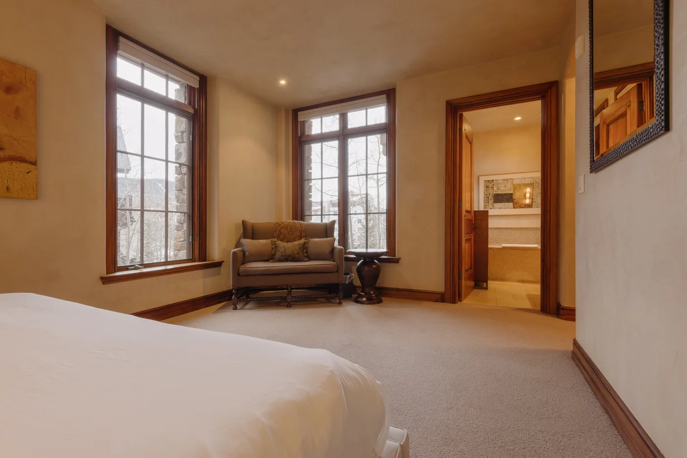 A bedroom with a bed, seating, and tall windows beside an open doorway.