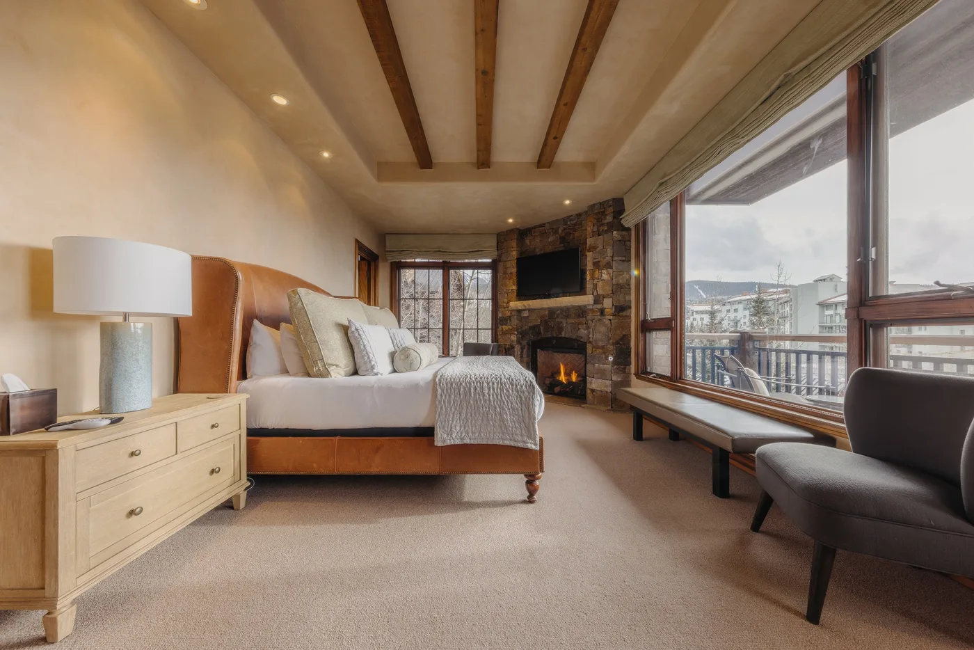 A bedroom with a bed, a fireplace, and large windows overlooking the mountains.