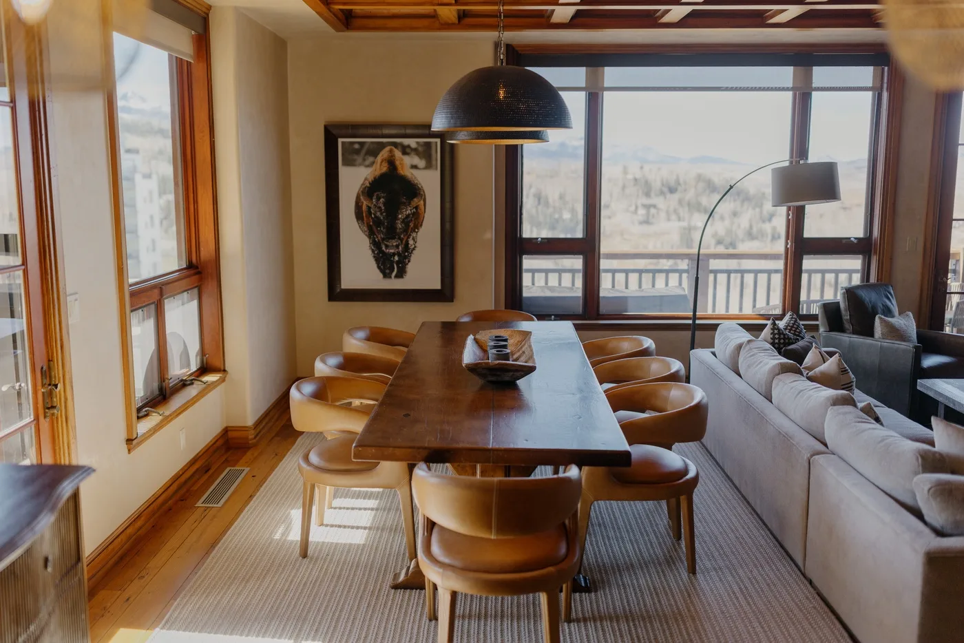 A dining area with a long wooden table and seating beside large windows.