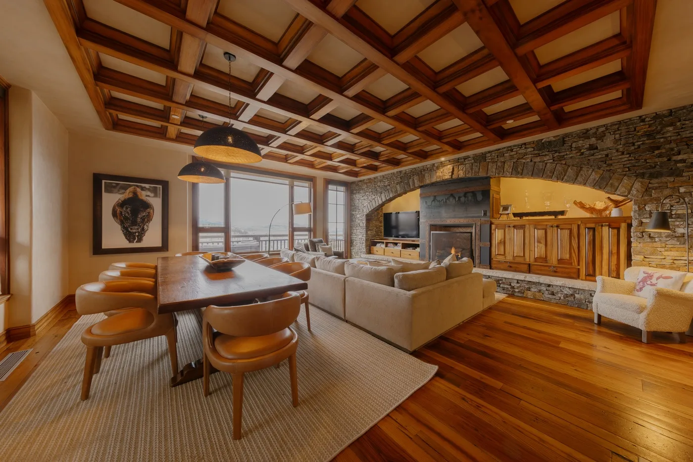 A spacious living and dining room with seating, a table, and a stone fireplace.