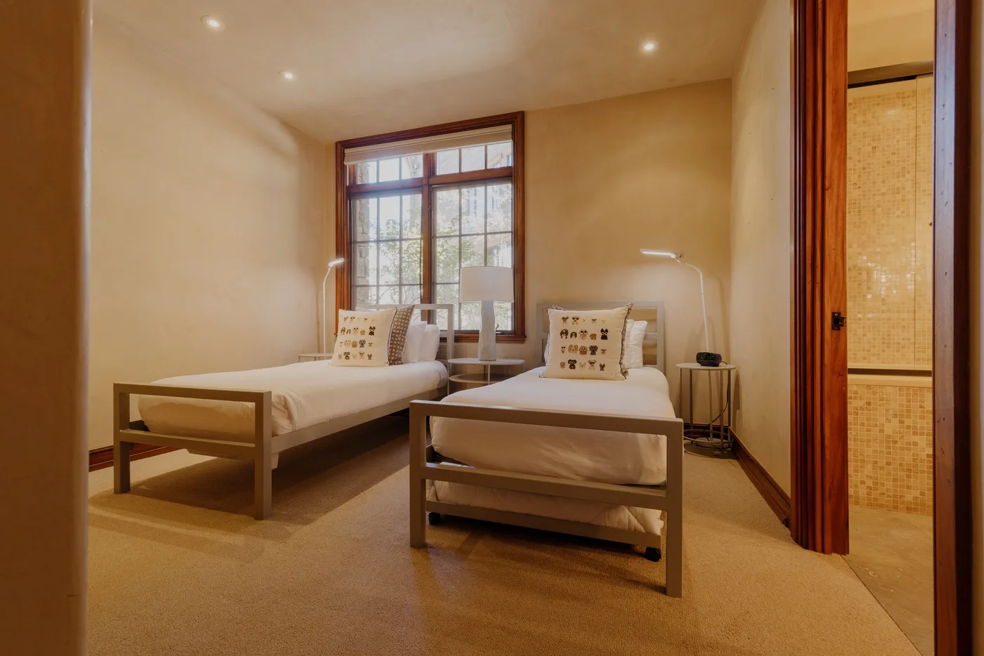 A bedroom with two beds beside a large window.