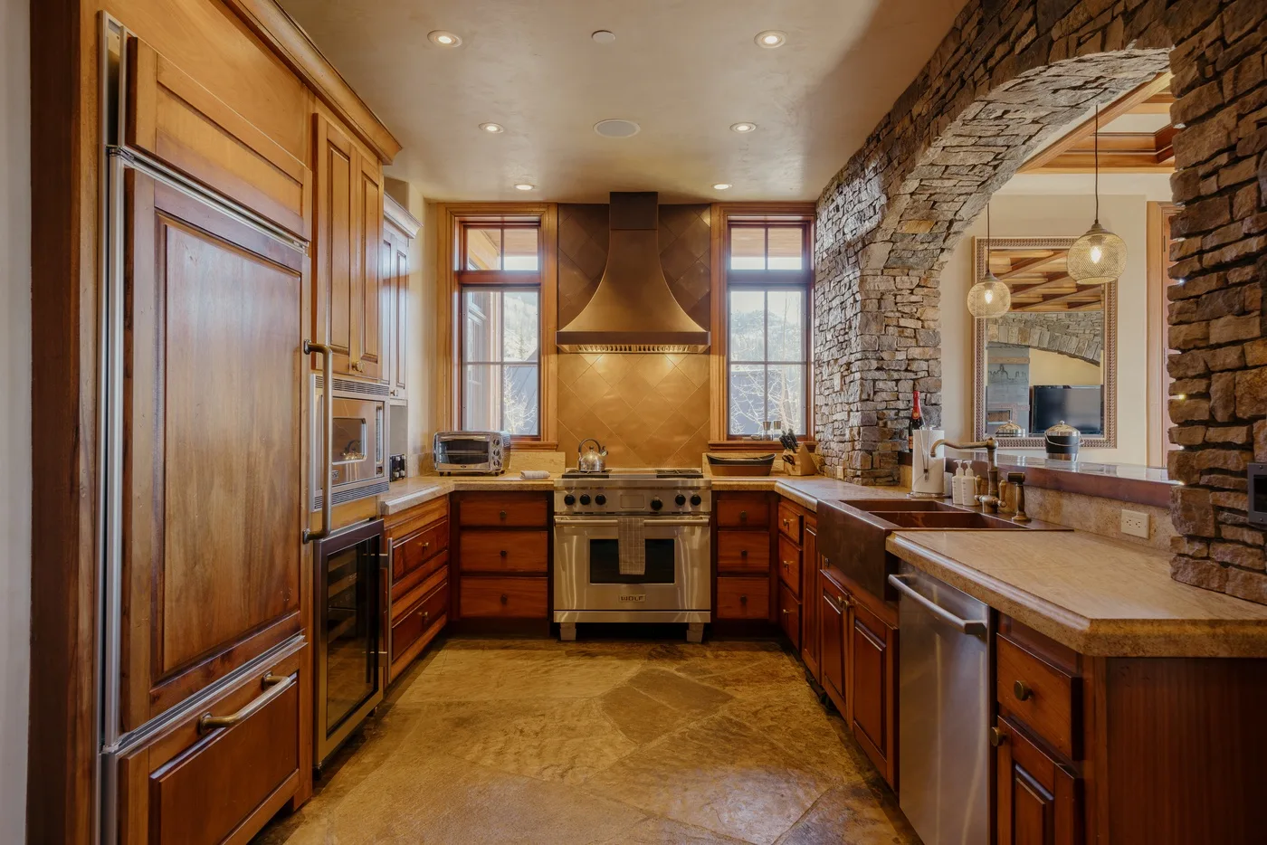 A spacious kitchen with wood cabinetry, a central range, and a stone archway.