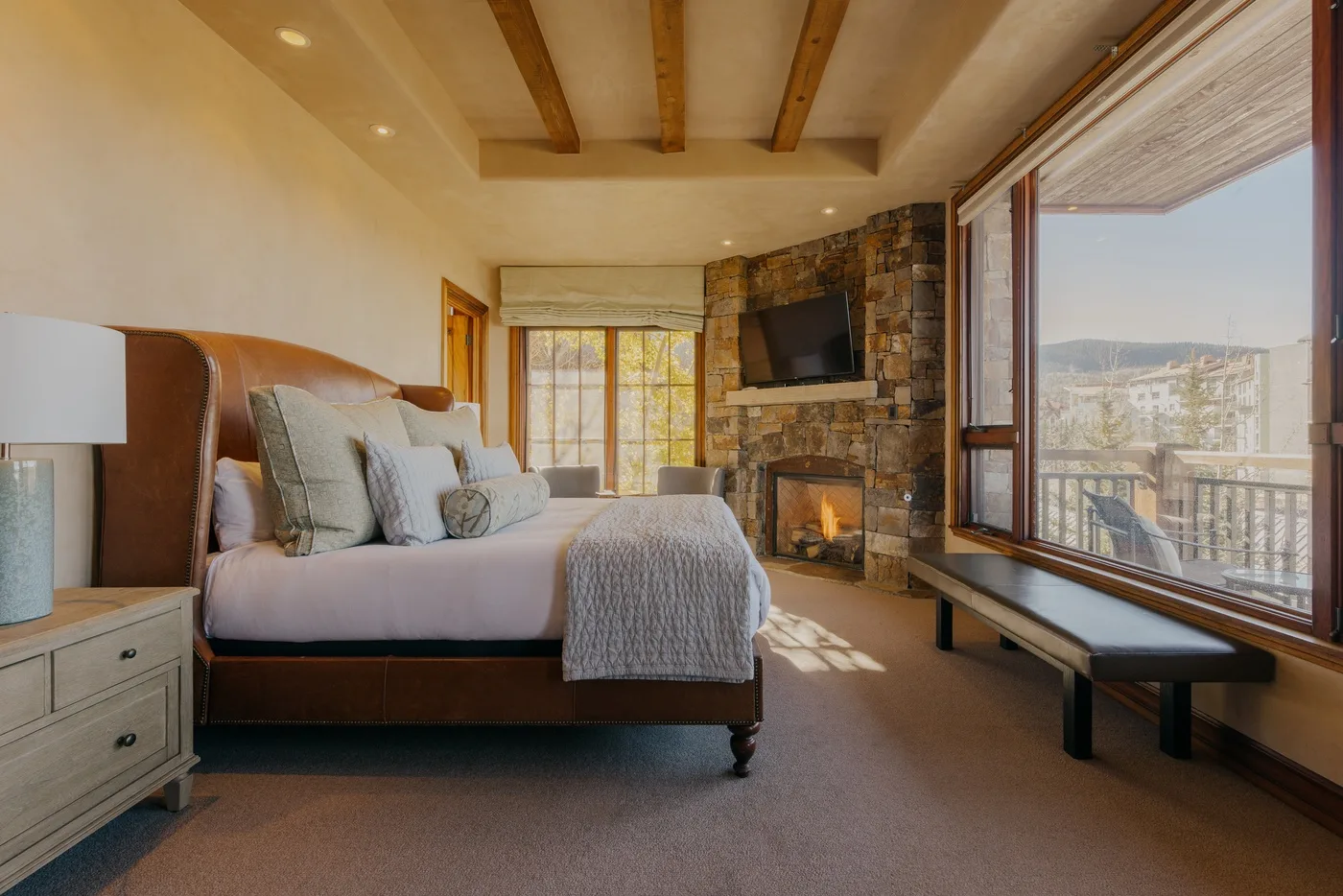 A bedroom with a bed, stone fireplace, and large windows overlooking the landscape.