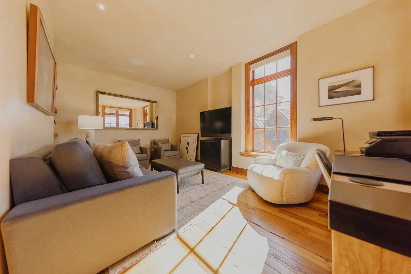 A bright living room with seating, a television, and a large sunlit window.