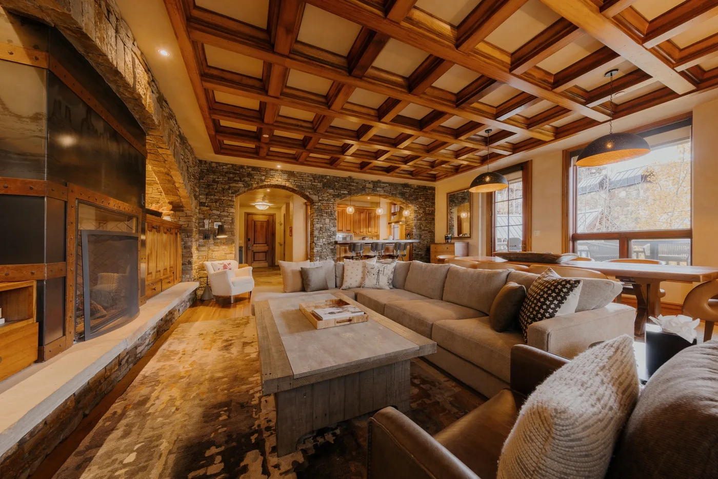 A spacious living room with sectional seating, a stone fireplace, and a wood-paneled ceiling.