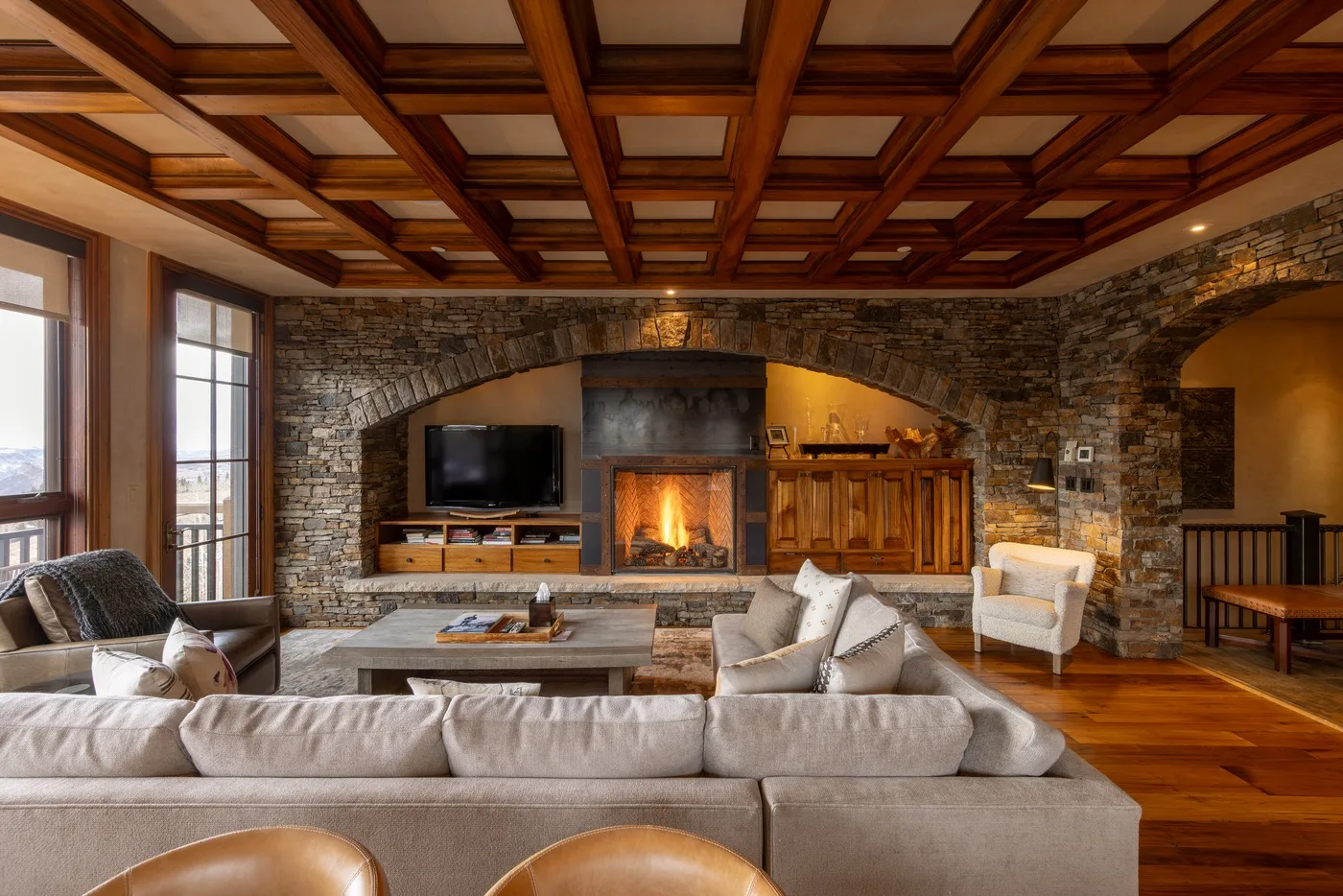 A spacious living room with seating, a stone fireplace, and a wood-paneled ceiling.
