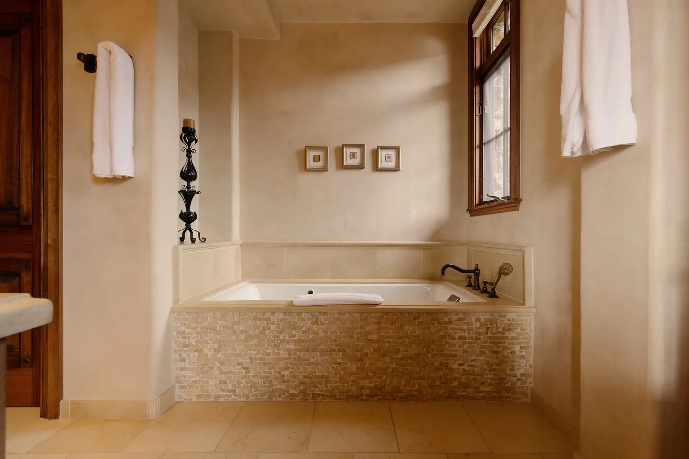 A bathtub sits in a beige tiled bathroom beneath a window.