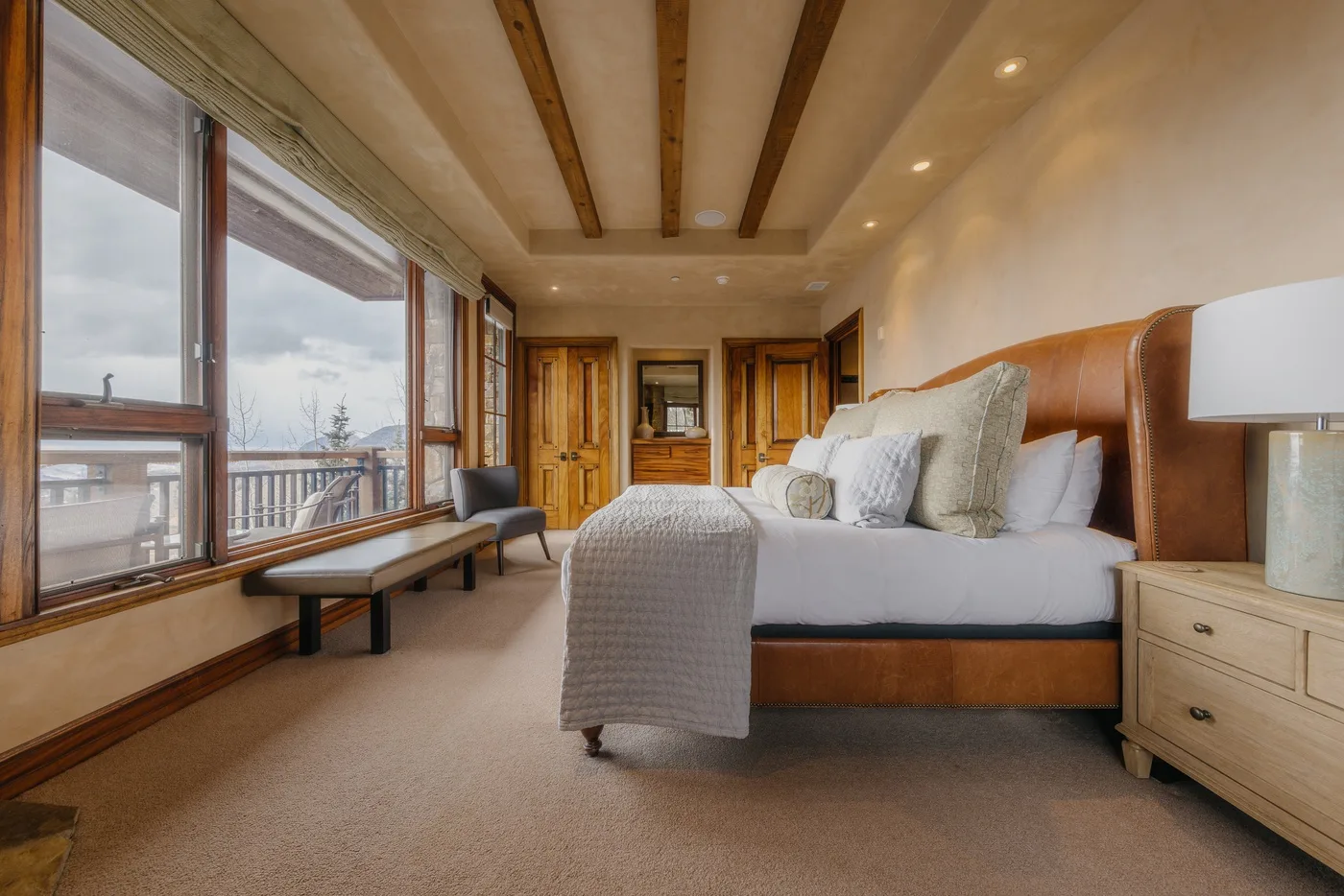 A bedroom with a large bed beside broad windows overlooking the outdoors.