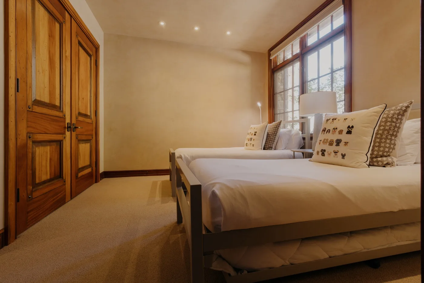 A bedroom with two beds beside a large window and wooden closet.