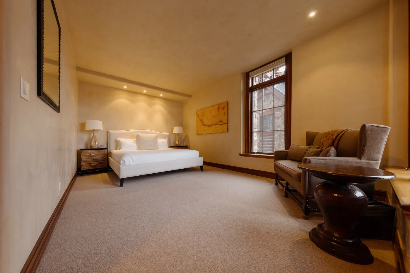 A bedroom with a bed, seating, and a tall window.