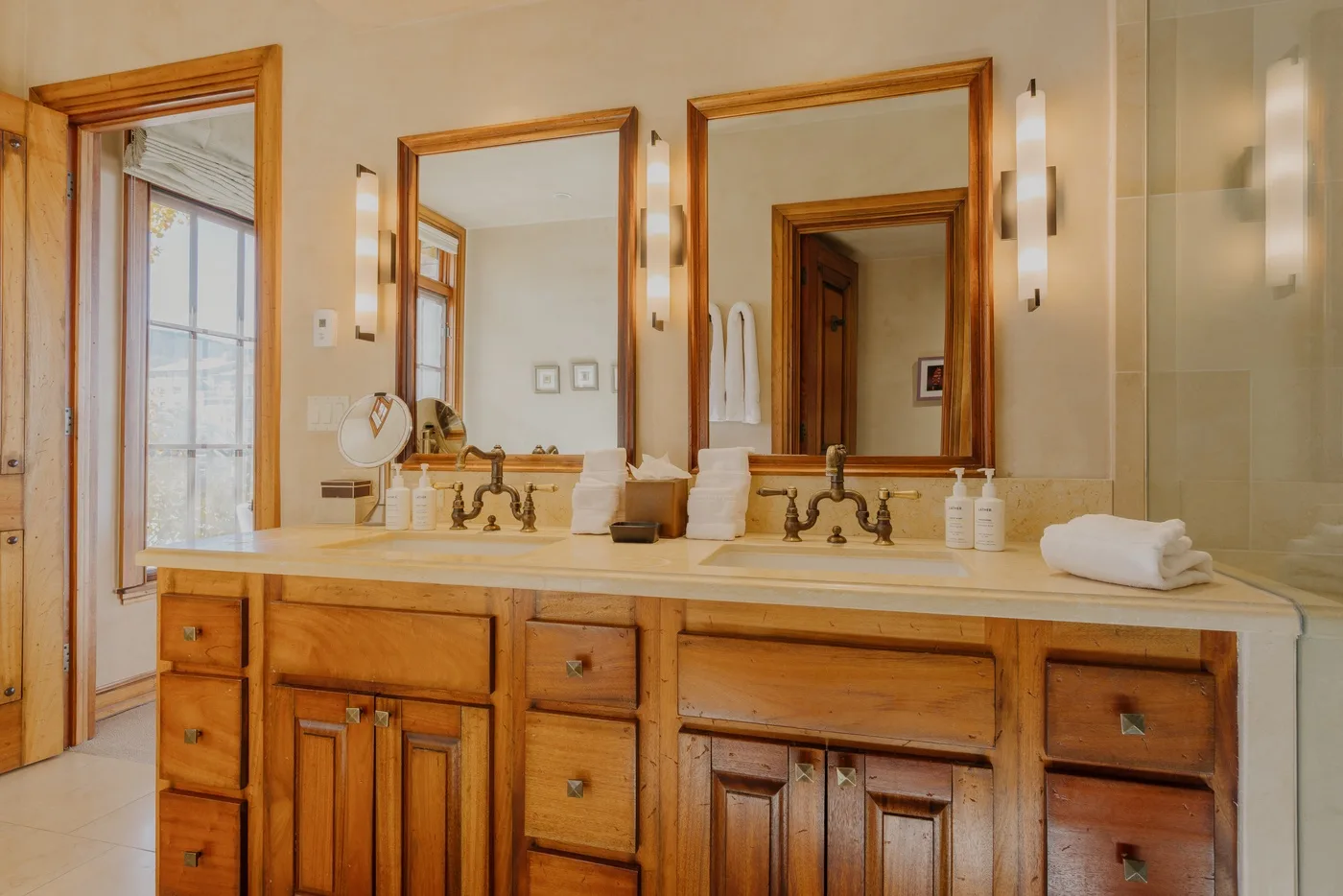 A bathroom vanity with twin sinks, wooden cabinetry, and large mirrors.