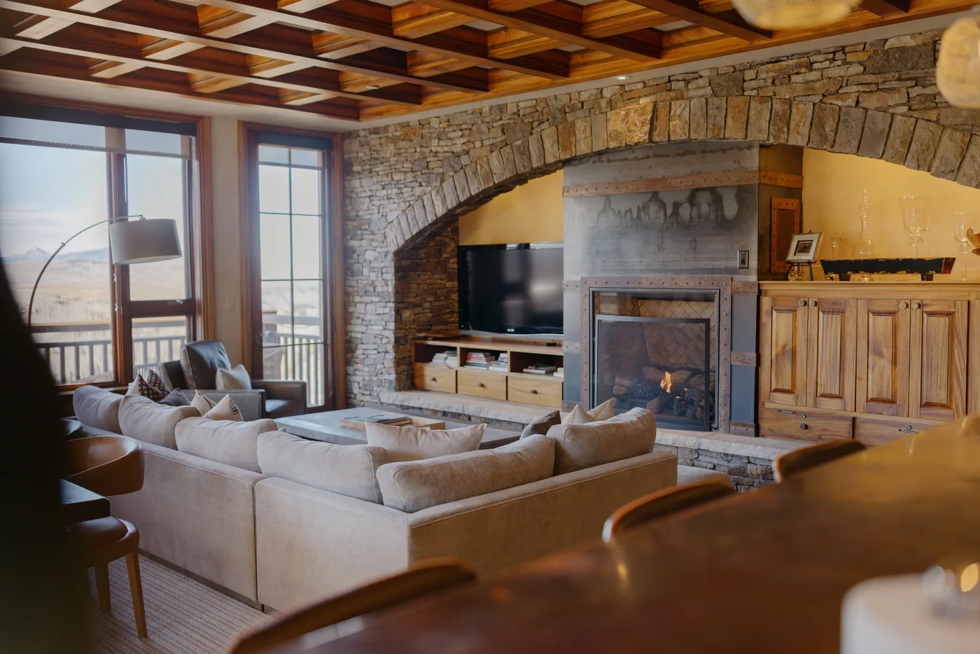 A living room with seating, a television, and a fireplace beneath a stone arch.