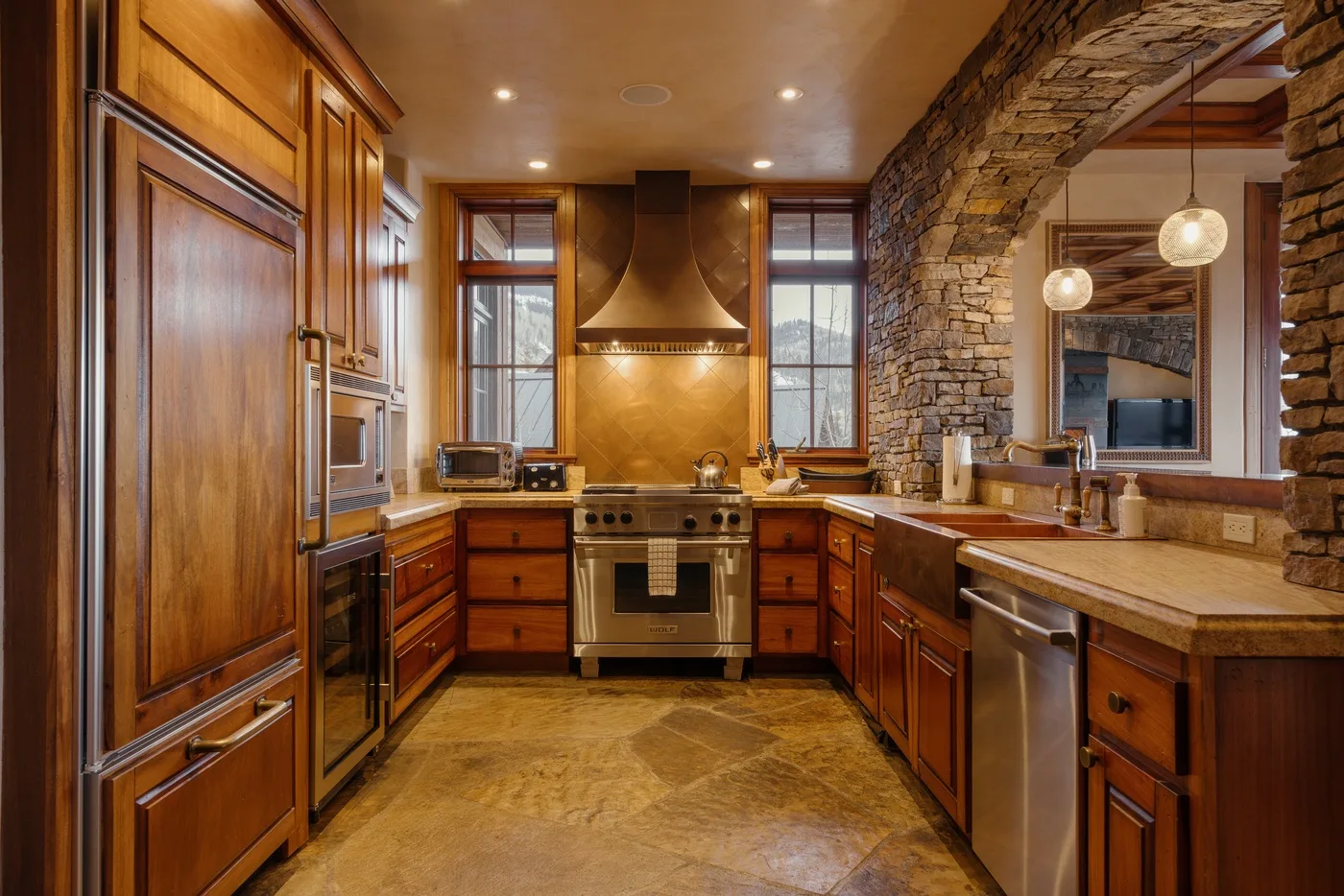 A spacious kitchen with wooden cabinetry, a central range, and stone walls.