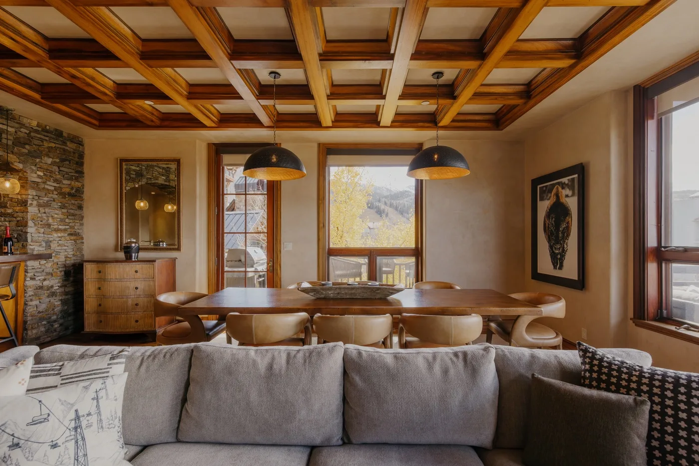 A dining area with a long wooden table and seating beneath a coffered ceiling.