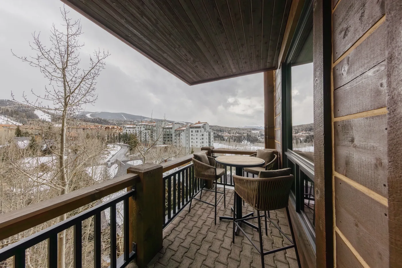 A covered balcony with outdoor seating overlooks a snowy landscape.